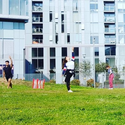 Three students dancing on the grass in front of Trinity Laban Creekside with red and white temporary fencing