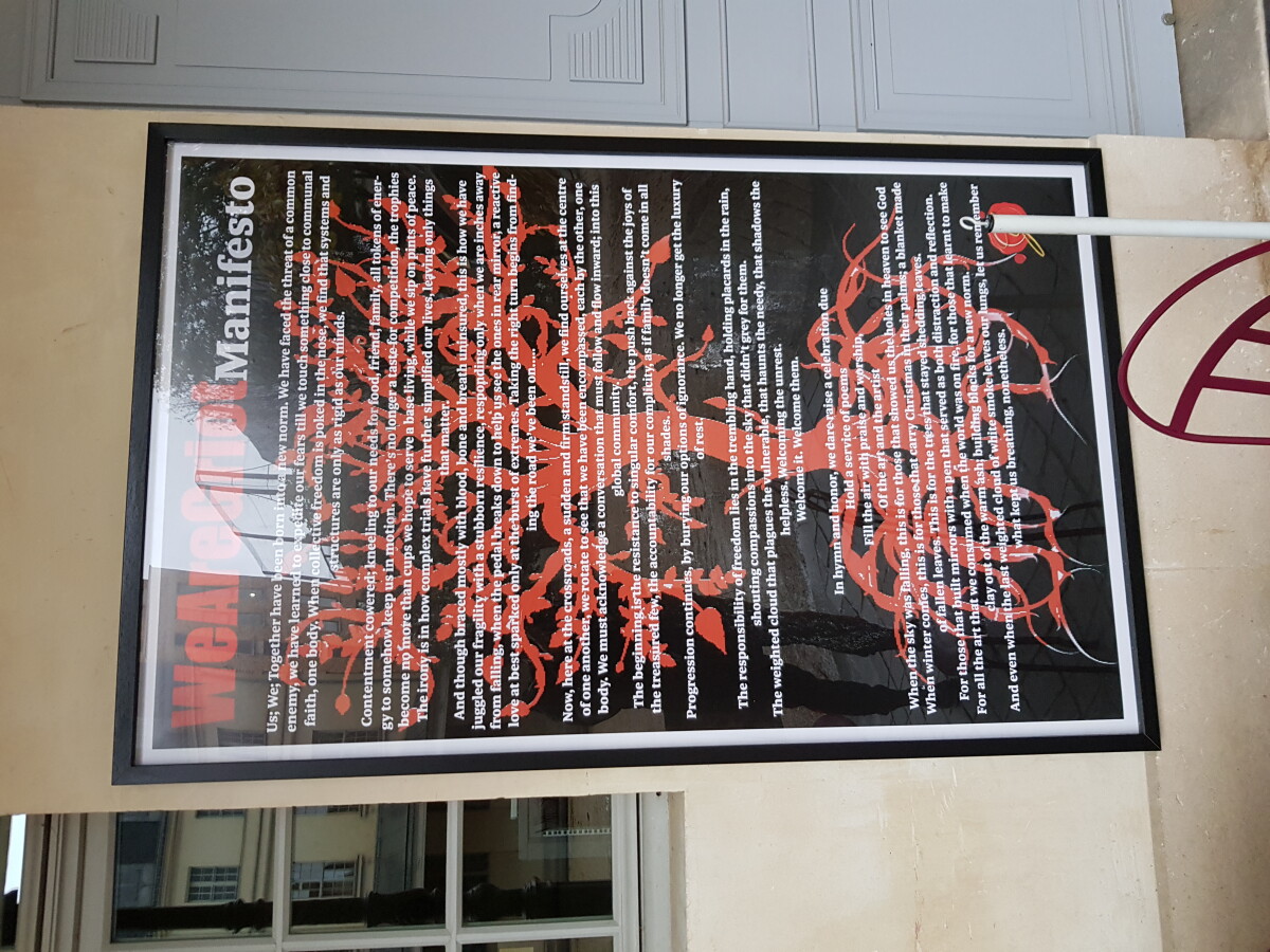 Image of a poster on a wall. The poster has a black background, a reddish image of a tree and roots and white text printed over