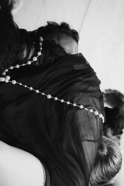 Two bodies merged and indistinguishable except for two glimpsed heads all wrapped in black silk with a string of pearls 