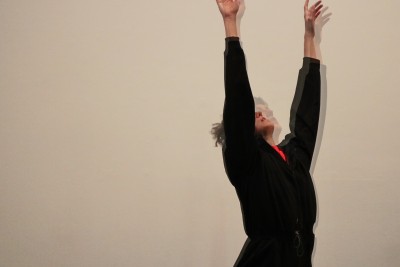 Female dancer in black with both arms raised and her face blurred 