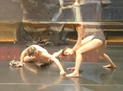 Digitally enhanced photo.  Two dancers in black briefs.  One wide legged and bent over, the other wide armed and lying on the floor.  The background is digitally blurred